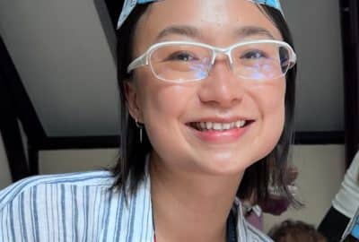 Photo of Lin, wearing glasses and a paper hat