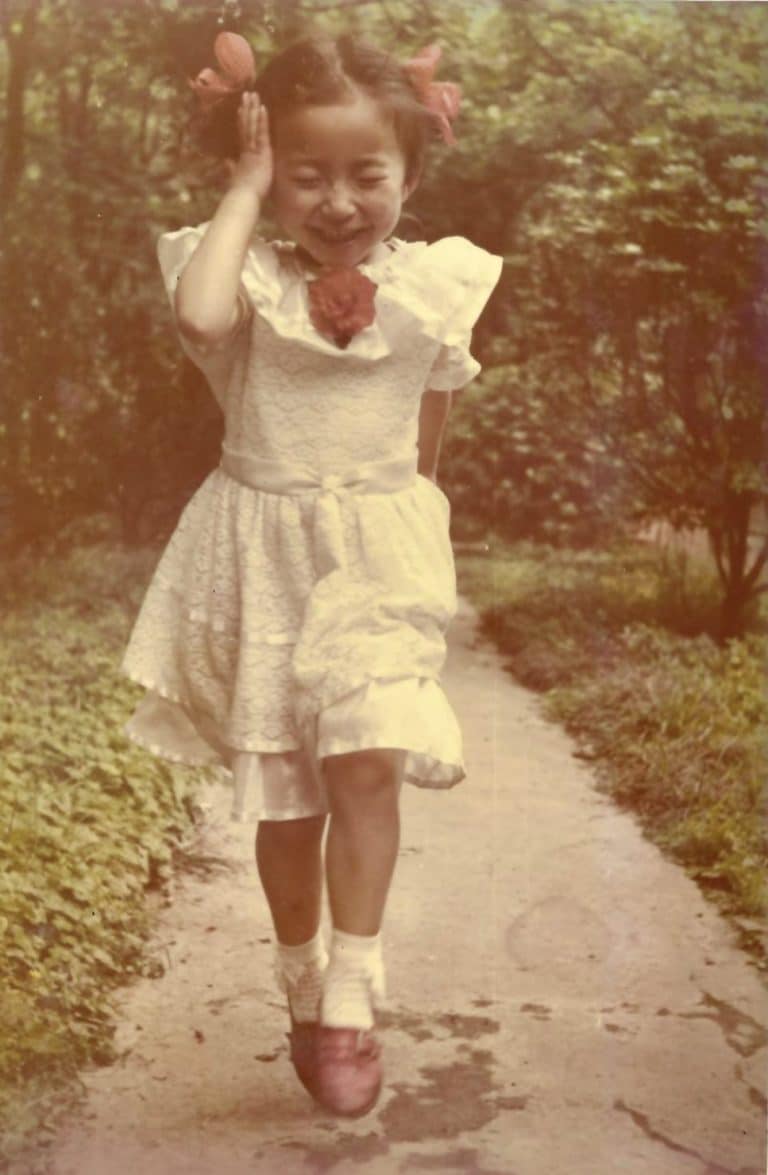 Lin Qiu, at 6 years old, running freely through the park, full of energy and joy, wearing a dress.